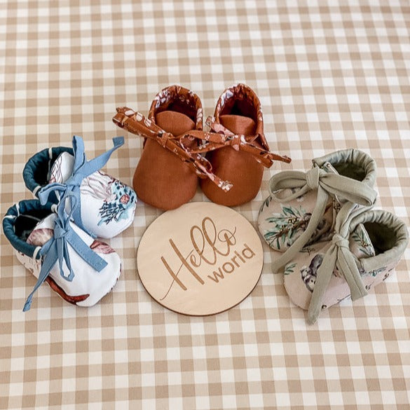 Three pairs of baby booties made from Snuggly Jacks Ocean Jersey Fabric on a baby bassing with an announcement disc