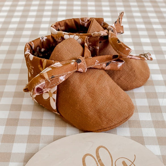 a Pair of Brown Linen baby booties with floral backing on a bench