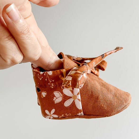 a Pair of Brown Linen baby booties with floral backing on a white backing