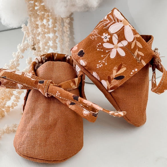 a Pair of Brown Linen baby booties with floral backing on a bench