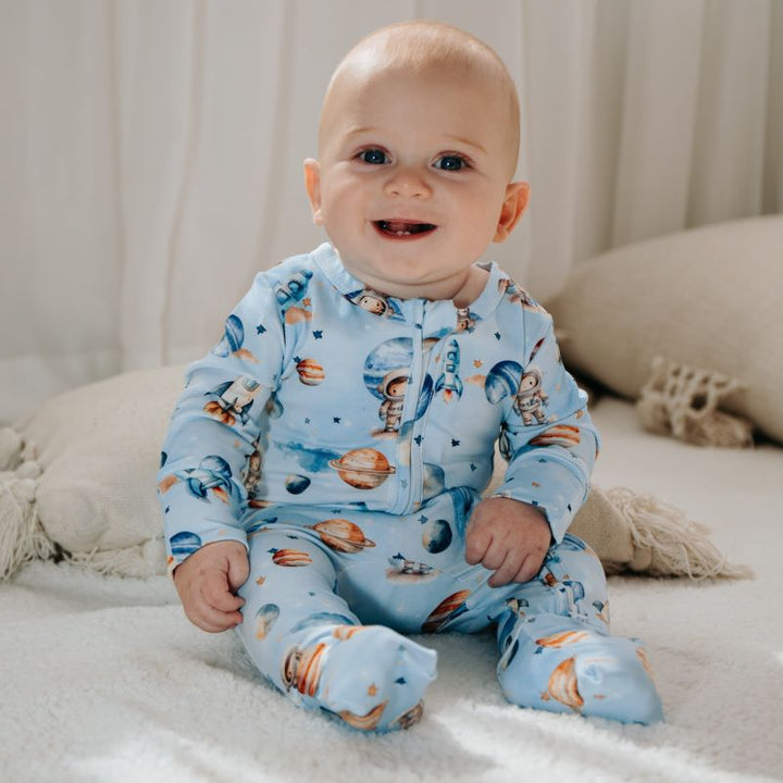 Baby sitting on a cozy blanket, dressed in a Space Rockets organic cotton onesie, showcasing a whimsical space-themed design.