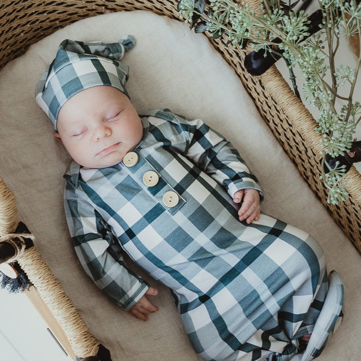 Baby wearing a knotted gown and a matching blue plaid beanie