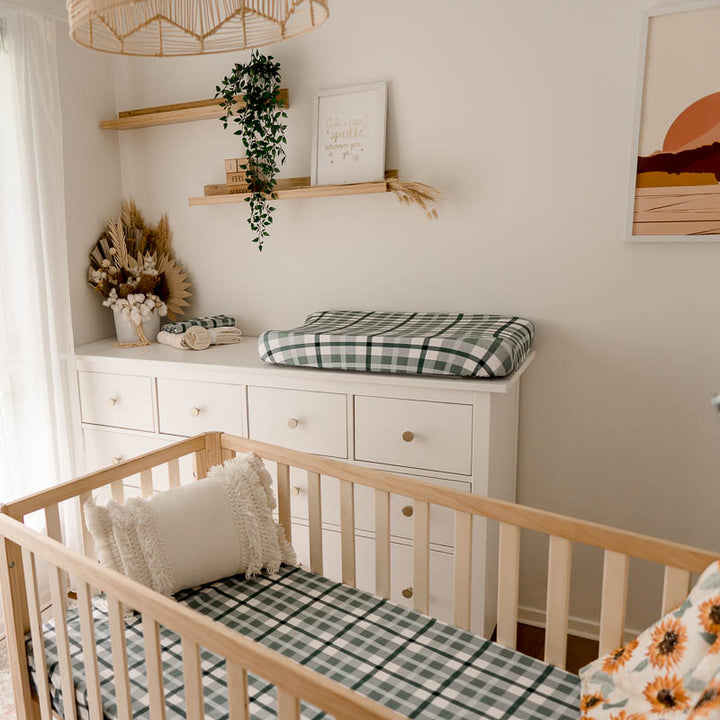 Full set of blue plaid items from snuggly jacks placed in a nursery with a sunflowers crib quilt hanging over the end of a pine crib.