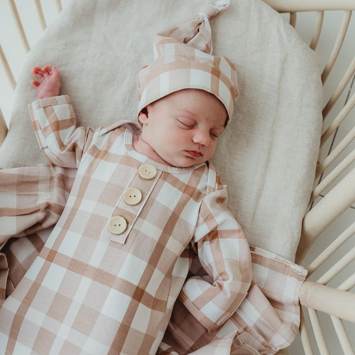 Sleeping baby in a bassinet wearing a knotted gown and matching beanie