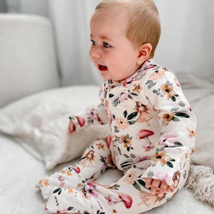 Smiling baby sitting on a cozy surface, wearing a Fairies and floral organic cotton onesie designed for comfort and style