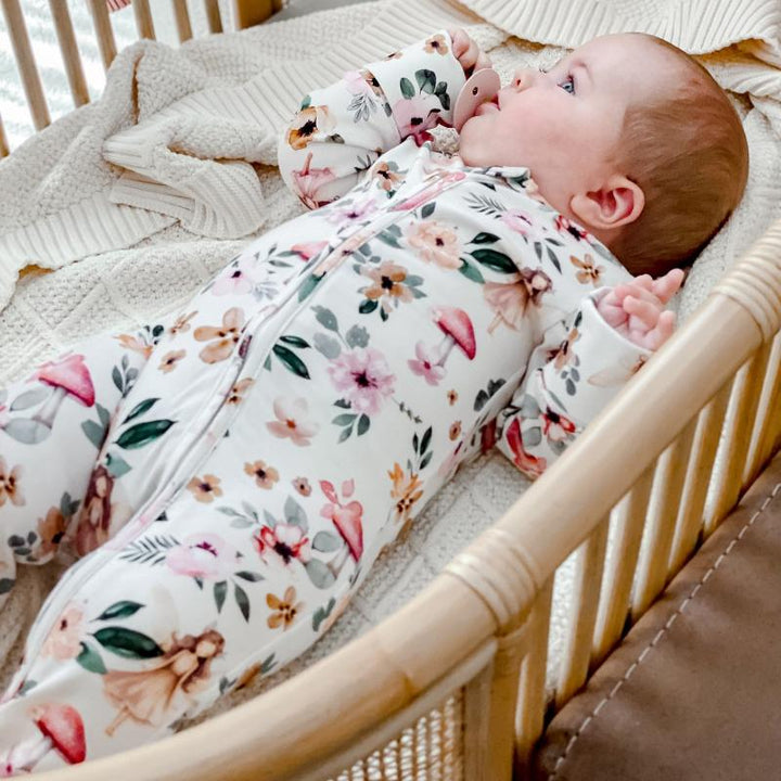 Baby lying in a bassinet, dressed in an organic cotton onesie with vibrant Fairies and floral print, perfect for creating a magical nursery