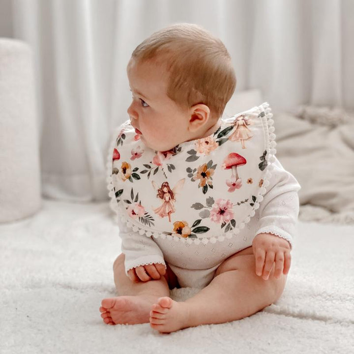 Baby wearing a Fairy Garden bib with delicate floral and fairy prints, crafted from soft organic cotton with an adjustable snap closure.