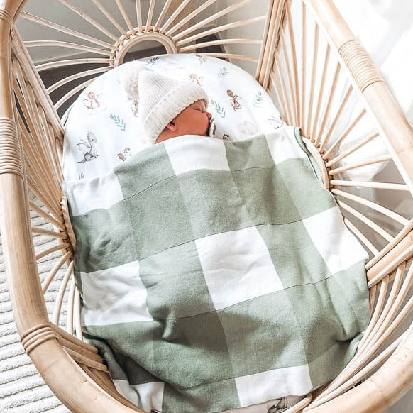 Green gingham cotton knitted blanket, being used by a baby in a ratan bassinet. Our blankets are breathable, soft, versatile and designed to last.