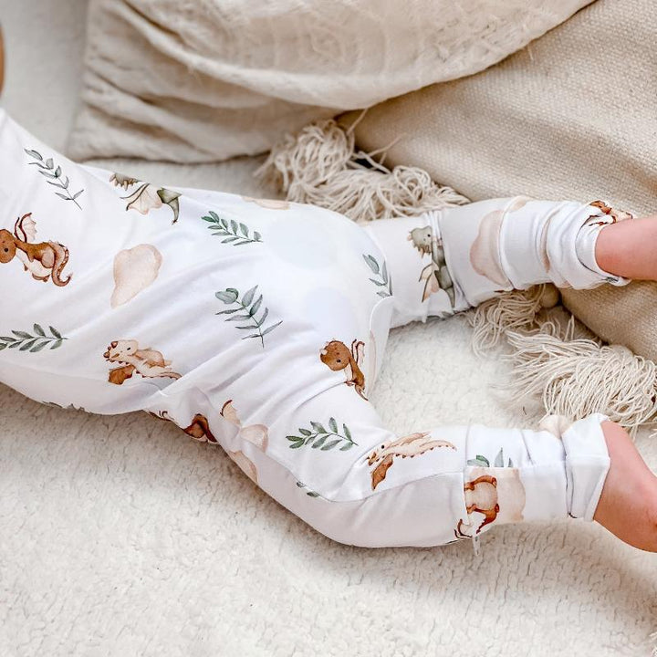 Baby lying on a soft surface in a Mystique dragon print organic cotton onesie, showcasing comfort and whimsical design for baby sleepwear