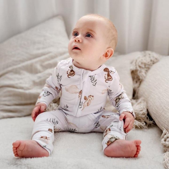 Baby sitting on a cozy blanket wearing a Mystique dragon print organic cotton onesie, perfect for matching stylish nursery decor.