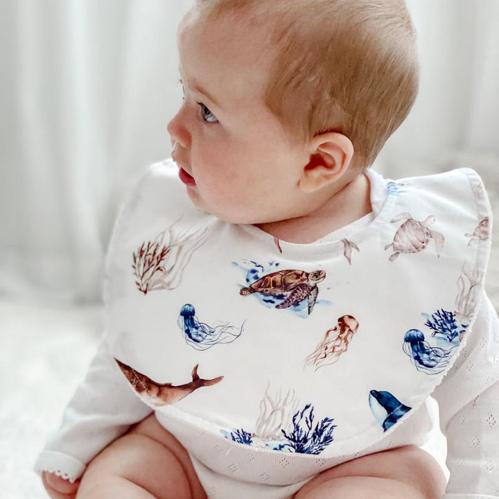 Close-up side view of a baby wearing an ocean-inspired organic cotton bib, highlighting the durable material and snug adjustable fastener.