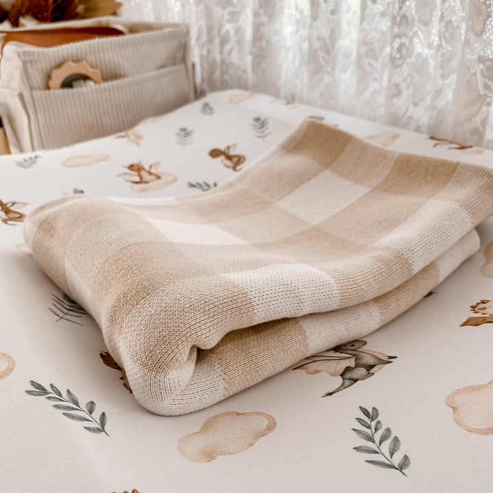 Soft sand gingham knitted baby blanket made from organic cotton, displayed on whimsical nursery bedding for cozy styling.