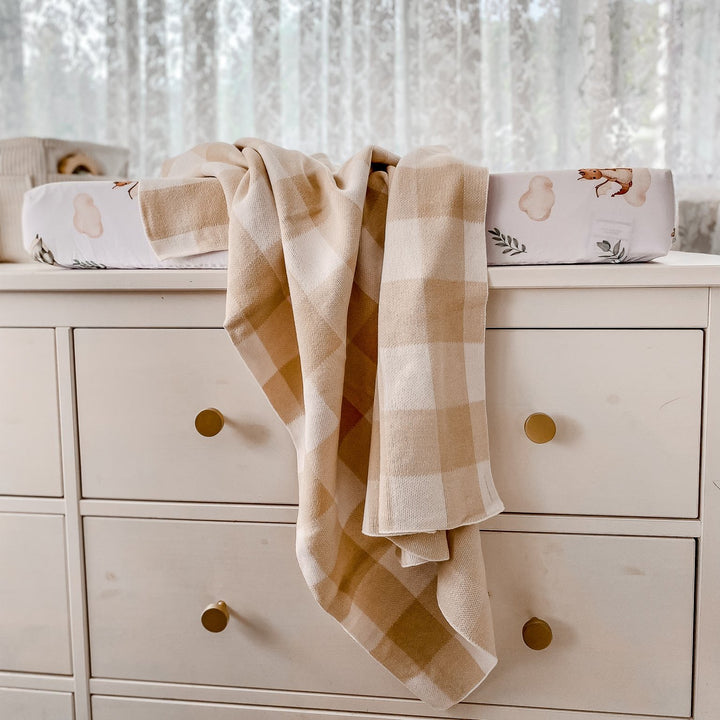 Sand gingham organic cotton baby blanket draped over nursery dresser, combining timeless style with cozy functionality.