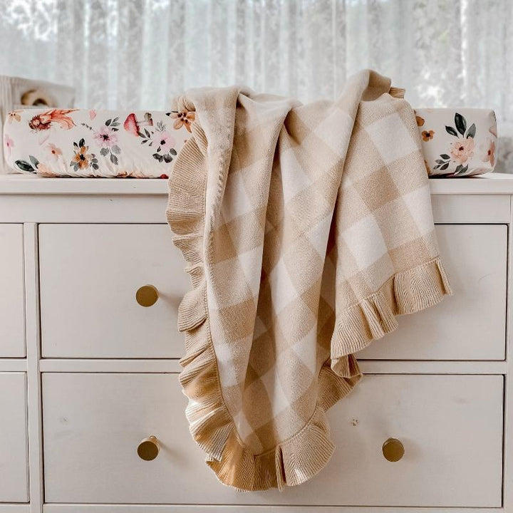 Sand gingham frill knitted baby blanket draped over a nursery dresser, made from breathable organic cotton for warmth and comfort.