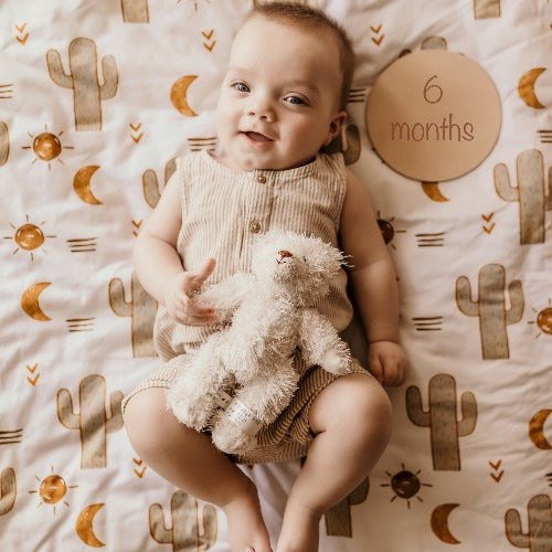 6 month old baby boy laying on a Snuggly Jacks Arizona fitted crib sheet holding his stuffed bear