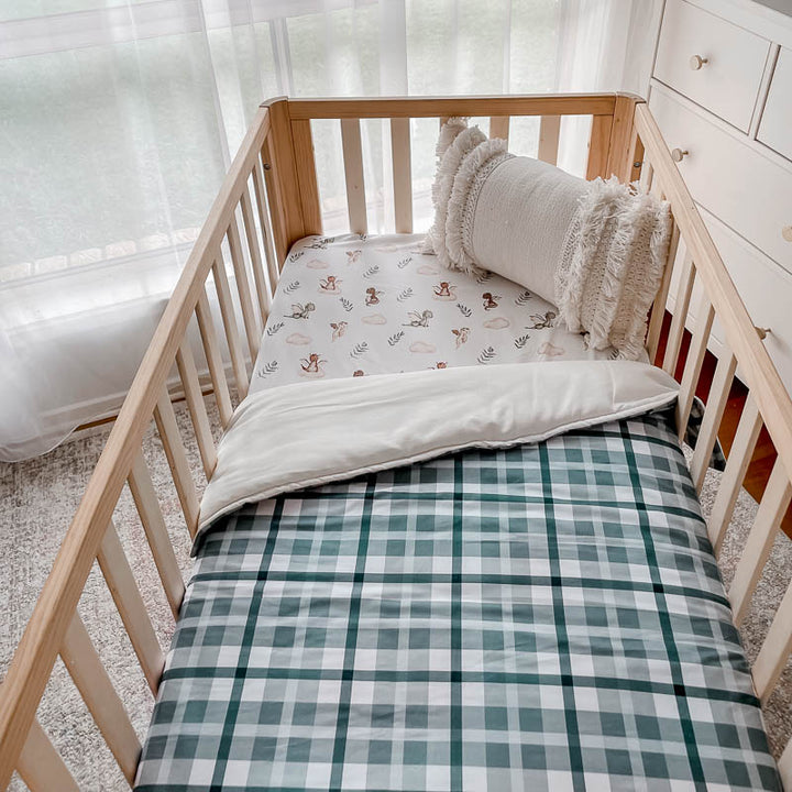 Side angle shot of a pine cot made up with cotton fitted sheet and a 100% cotton cot quilt