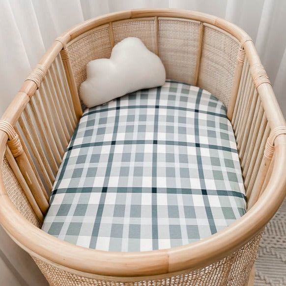 Rattan bassinet made up with a blue plaid cotton sheet and a cute little cloud pillow in the far end