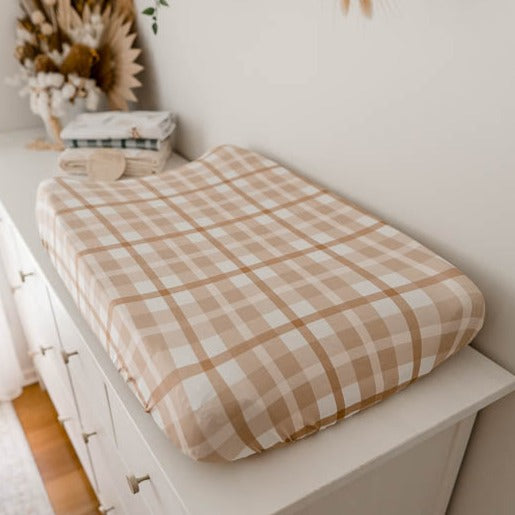Change table pad covered with a brown plaid cover and set on a table with burp cloths in the background