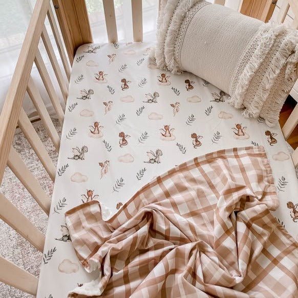 Pine crib made up with a cotton fitted crib sheet with a brown plaid dimple dot minky blanket laid across it