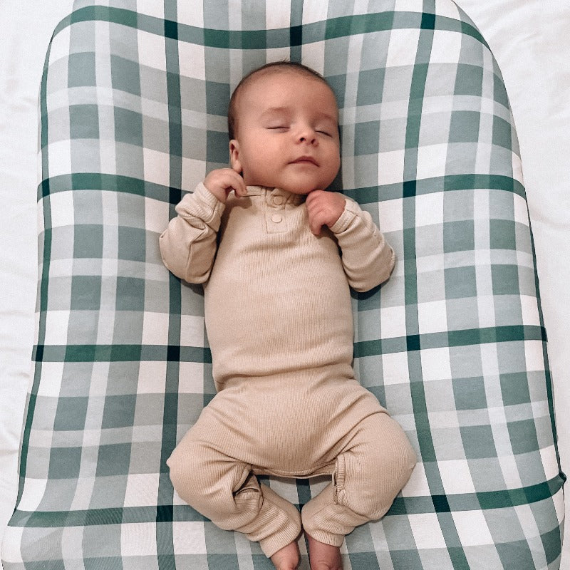 A sleeping baby using a baby lounger from snuggle me organic covered by a blue plaid change pad cover