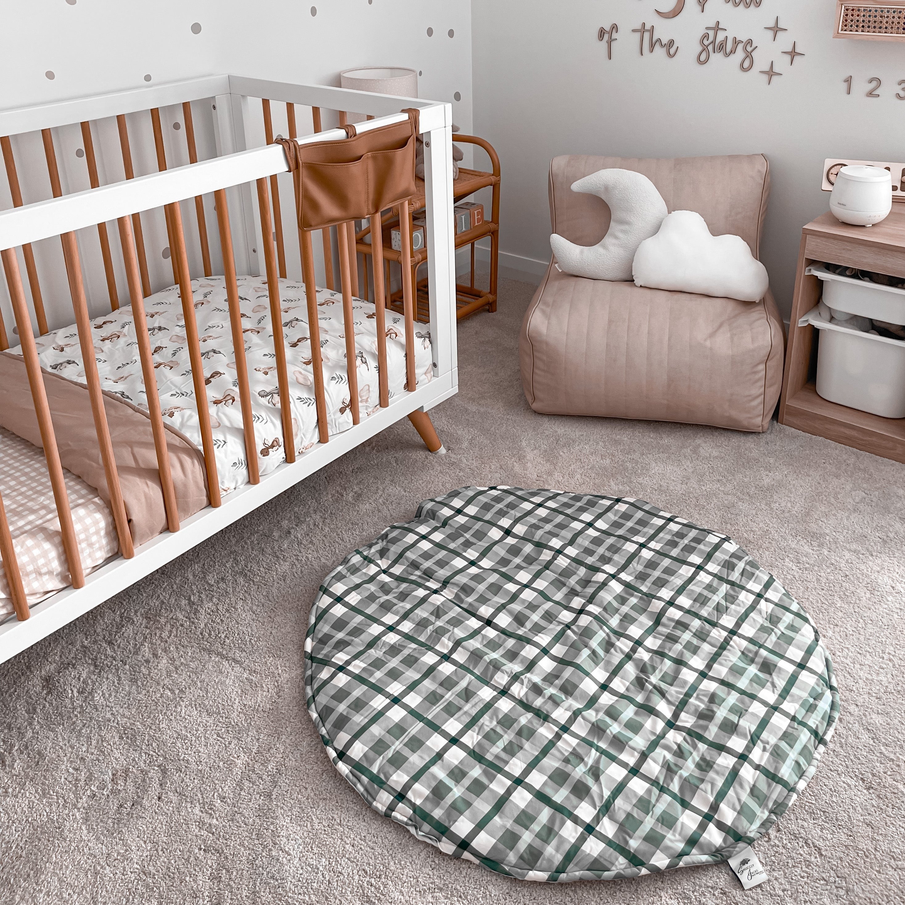 Nursery with grey carpet, pine crib with white features and a rattan bedside table showcasing the blue plaid playmat from snuggly jacks canada