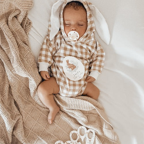 Newborn baby laying on a bed with a bunny outfit and snuggly jacks organic taupe knitted blanket