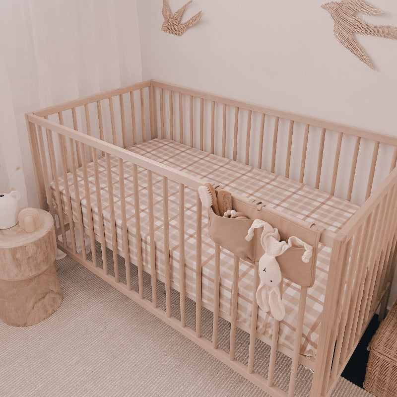 crib set in the corner of a nursery with a plush bunny hanging off the front side, rattan birds on the wall and a snuggly jacks cotton fitted sheet on the mattress.