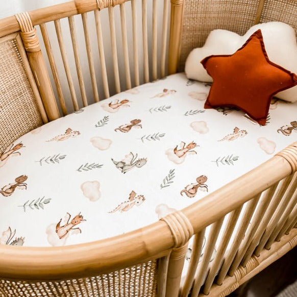 Close up of a white bassinet sheet with dragons, leaves and clouds on it in a stylish pattern