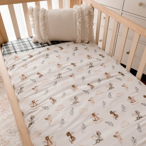 Pine crib made up with a blue plaid fitted sheet and a white cot quilt with dragons, leaves and clouds printed on it.