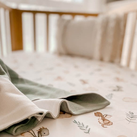 Pine crib, sheet with dragons and leaves, a green plaid cotton blanket