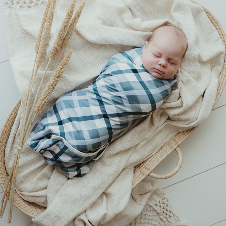 Adorable baby wrapped in a blue plaid wrap laying on top of a cotton blanket in a moses basket