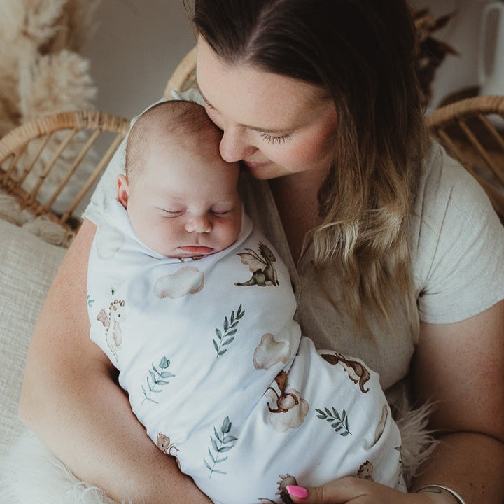 Baby in his Mother's arms wrapped up in a dragon print jersey swaddle wrap.