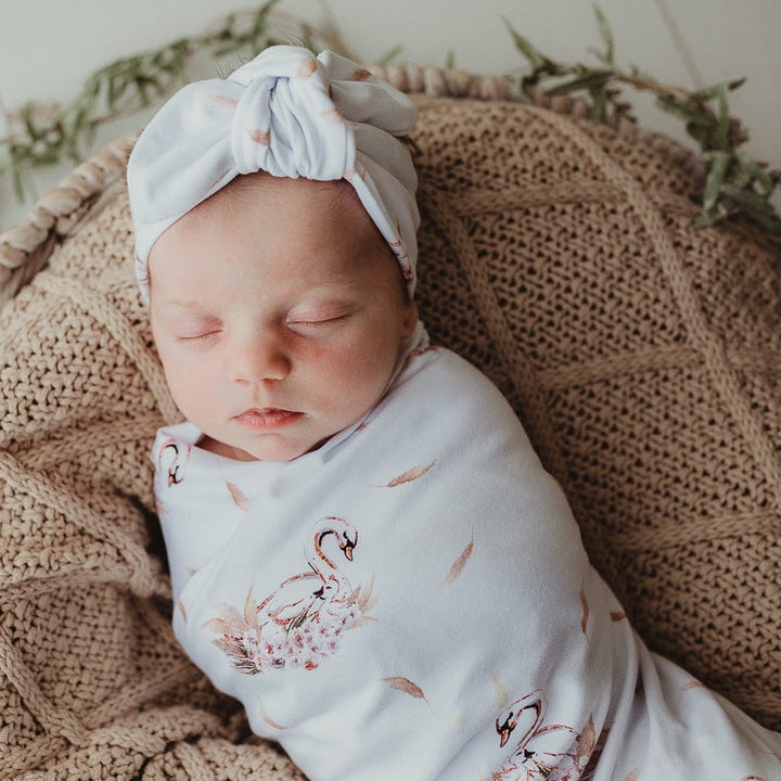 Baby sleeping while snug in a jersey stretch swaddle wrap and laying on a cotton knitted blanket.