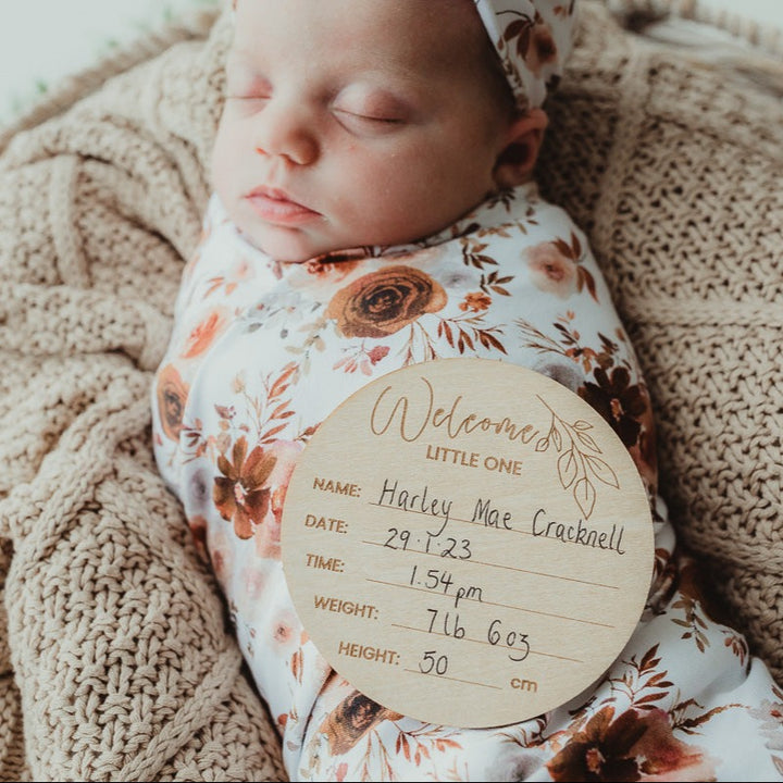 Snuggly swaddled baby with an announcement disc sleeping on top of a cotton blanket