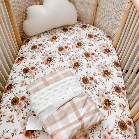 Rattan bassinet with a floral cover made from cotton, presented with a snuggly jacks dimple dot minky blanket placed on top.