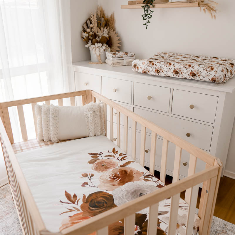 modern nursery with a crib set using a crib quilt with a large floral print and in the back ground a change pad with a warm floral printed change pad cover.