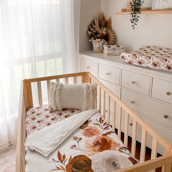 Wide shot of a nursery with fitted cot sheets, burp cloths, change mat covers and cot quilt all in a willow floral style print.