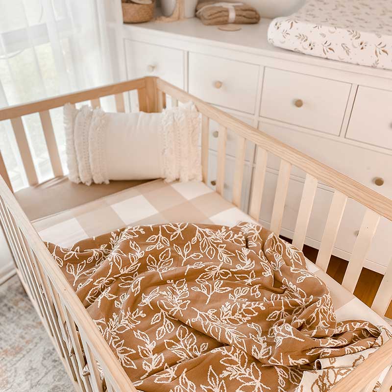 Baby Nursery with wooden crib and an Snuggly Jacks Foliage Sand Reversible Organic Knitted Blanket on the crib mattress